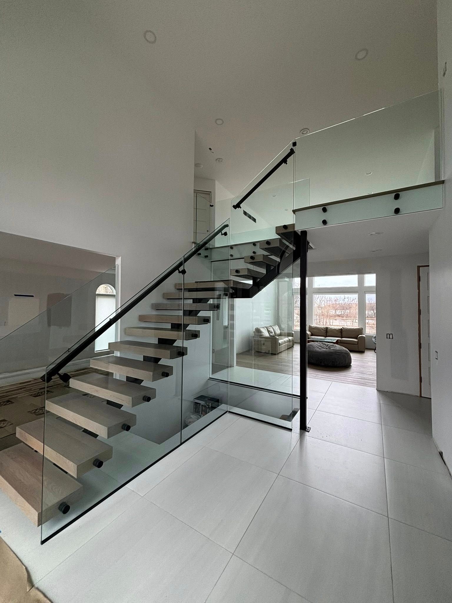 Modern home interior with floating staircase, glass railing, and white tile floor