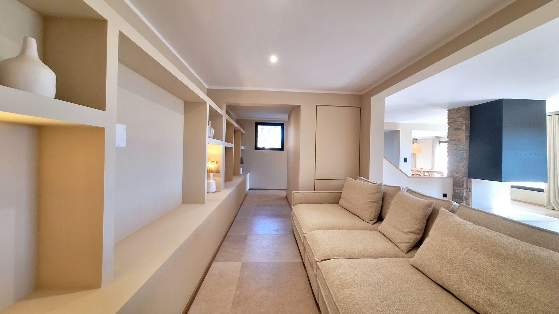 Salon étroit avec des étagères intégrées d'un côté, un canapé de l'autre et une vue dégagée sur une autre pièce.