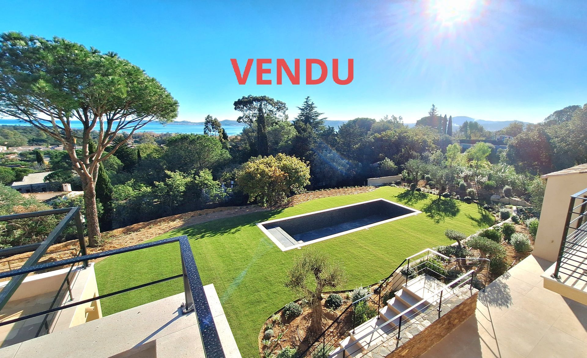 Panneau Vendu sur une vue panoramique d'une cour avec une piscine, de la verdure et un plan d'eau lointain.