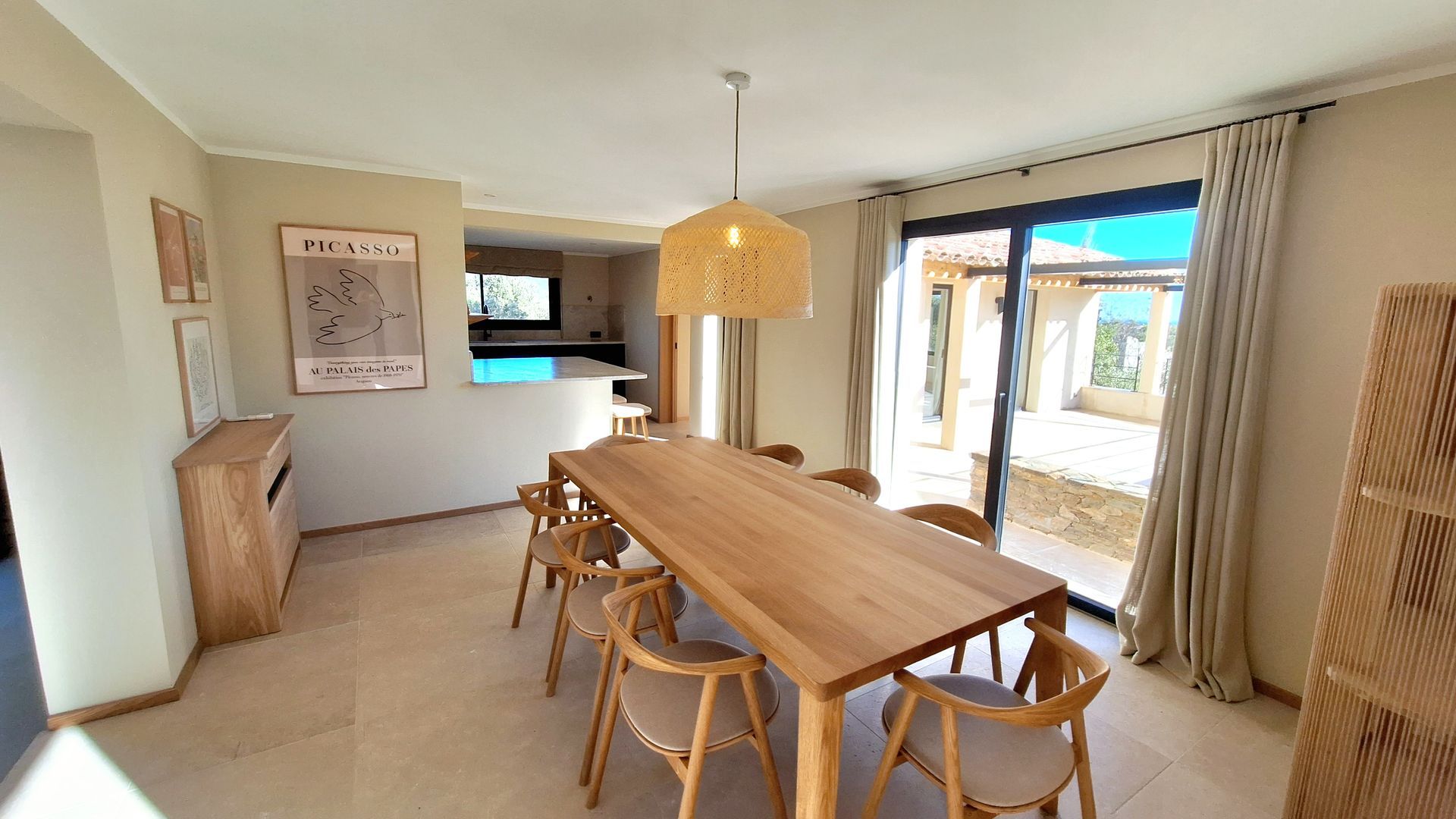 Salle à manger avec longue table en bois, chaises et porte coulissante en verre donnant sur le patio.