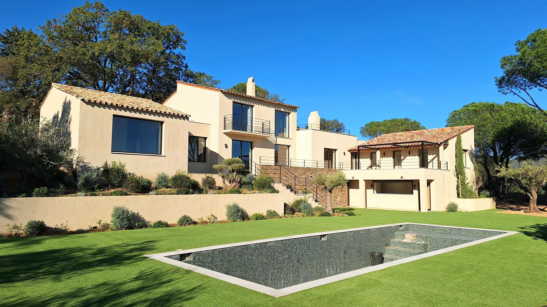 Villa beige avec piscine sur une pelouse herbeuse sous un ciel bleu clair.