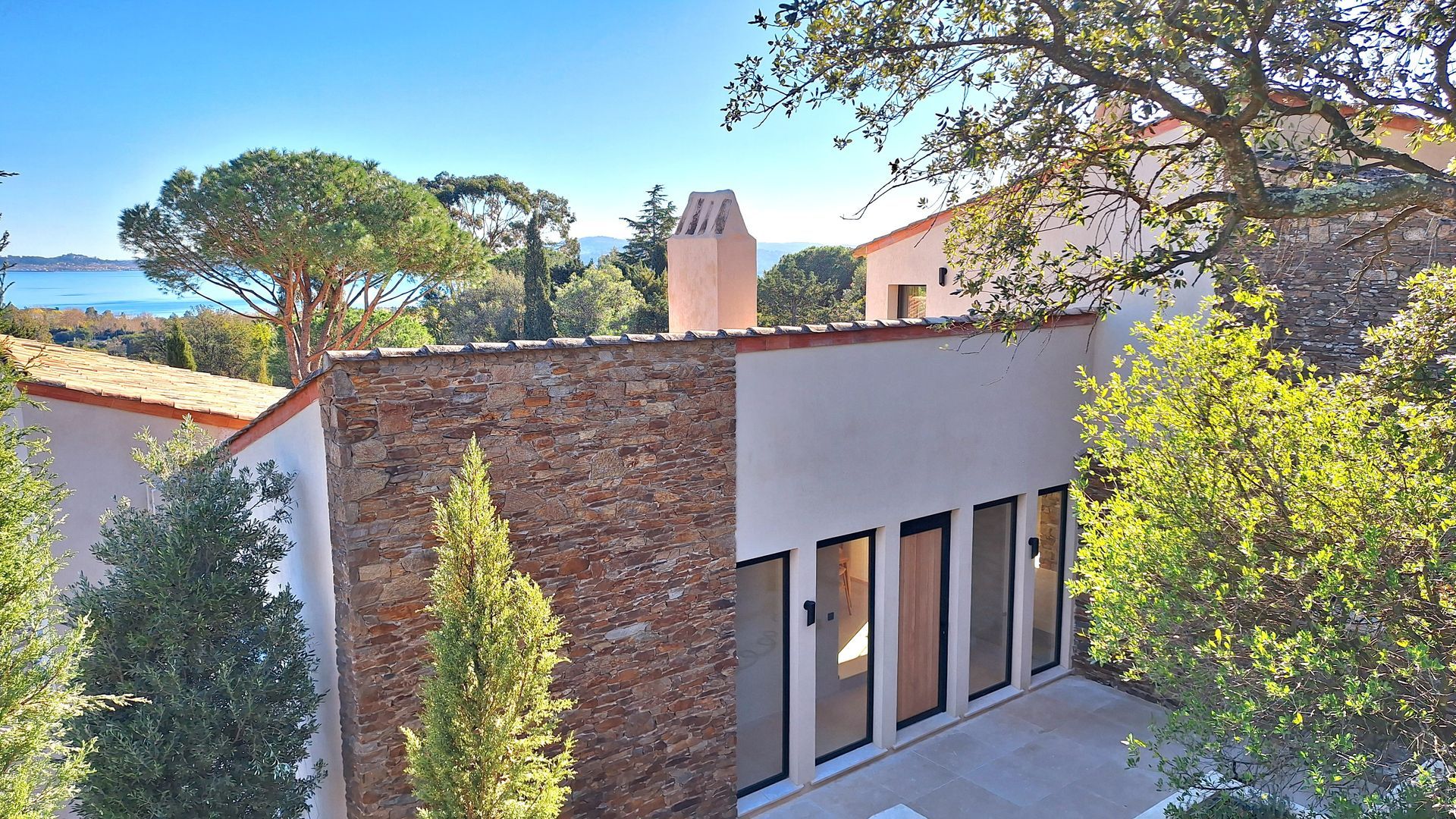 Extérieur d'une maison moderne avec mur en pierre, portes vitrées et toit en tuiles