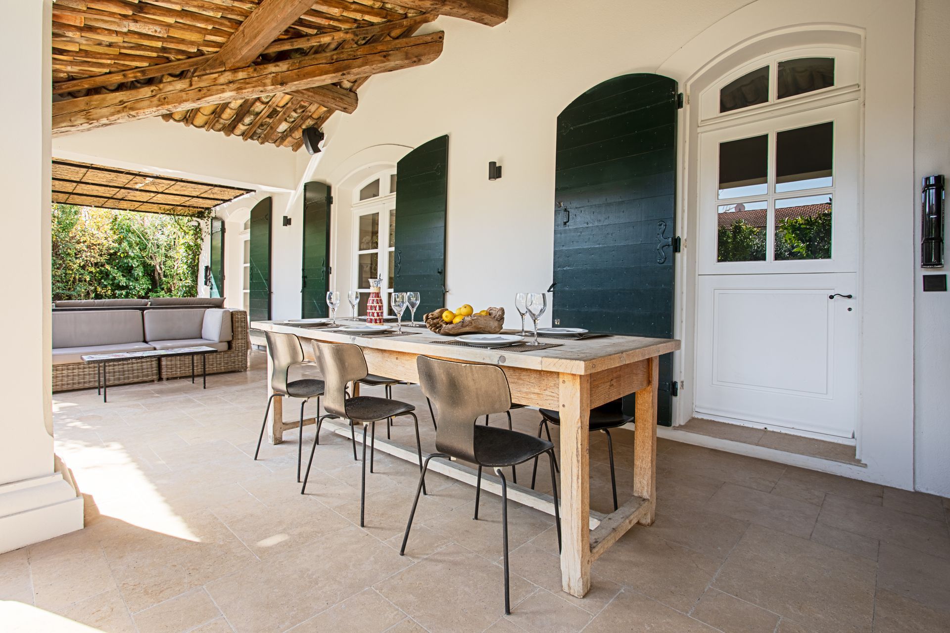 Terrasse couverte avec table en bois pour les repas et volets verts.