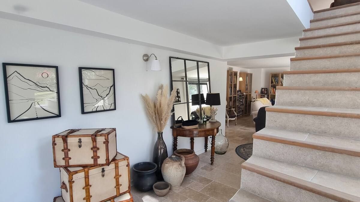 Une entrée lumineuse avec un escalier, des malles empilées, des œuvres d'art et des objets décoratifs.