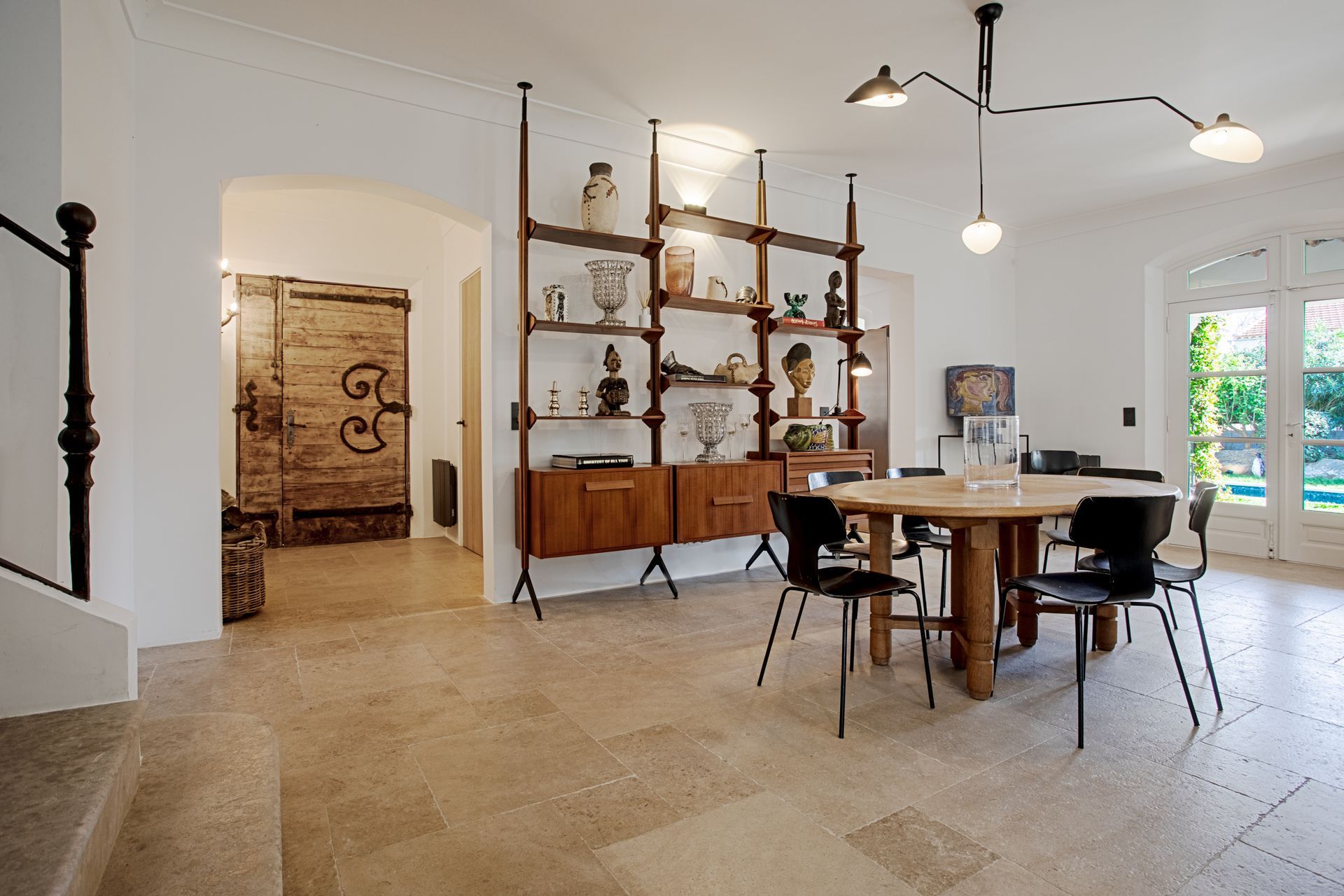 Salle à manger lumineuse et aérée avec table ronde en bois, chaises noires et étagère avec ornements