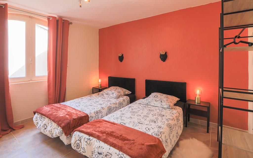 Chambre avec deux lits jumeaux, un mur d'accent orange et une fenêtre avec des rideaux rouges.