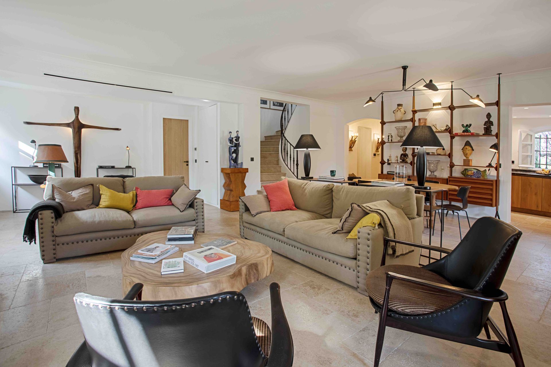 Salon lumineux avec deux canapés beiges, une table basse en bois et des fauteuils noirs.