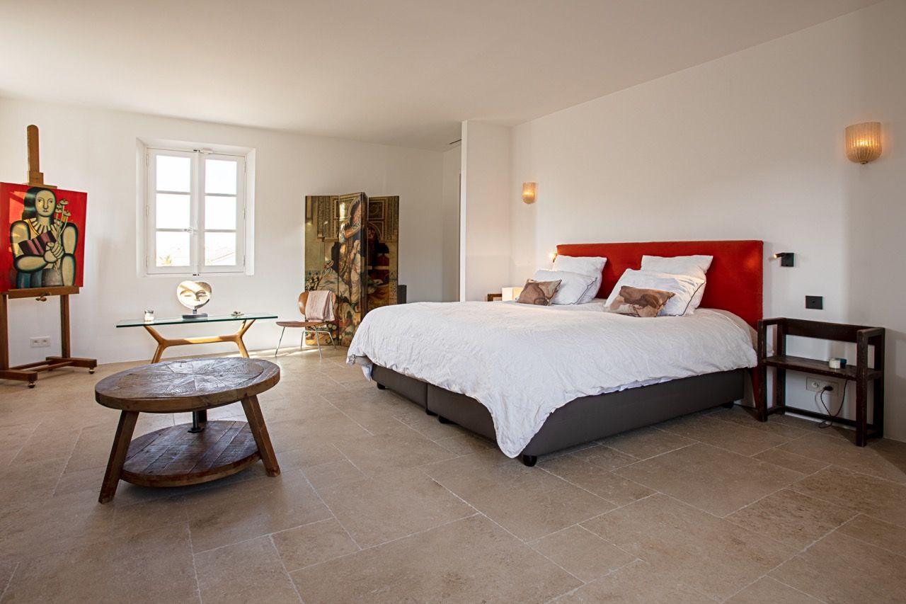 Chambre spacieuse avec un lit, des œuvres d'art et une table ronde. Murs blancs et lumineux et sol beige.