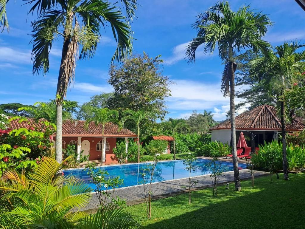 Piscine dans un cadre tropical ; un bâtiment au toit de tuiles rouges se dresse en arrière-plan. Couverture de piscine bleue. Étiquette « CO-EXCLUSIVITÉ ».