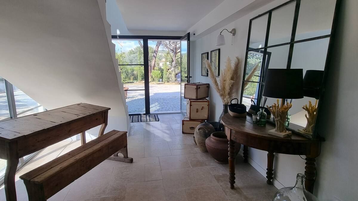 Entrée avec escalier, console, grand miroir et porte vitrée donnant sur une cour.