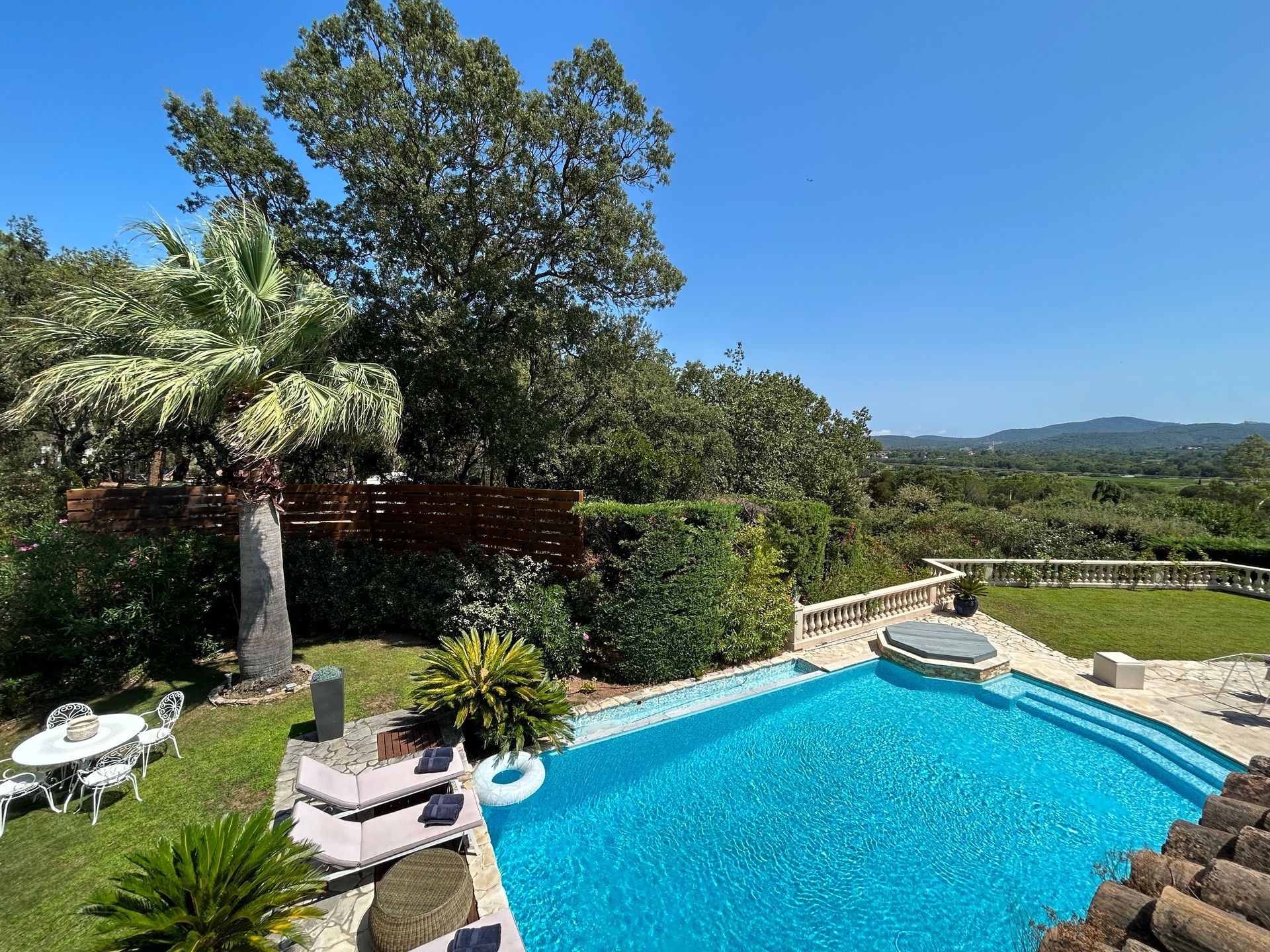 Piscine entourée d'arbres verts et de pelouse sous un ciel bleu vif.