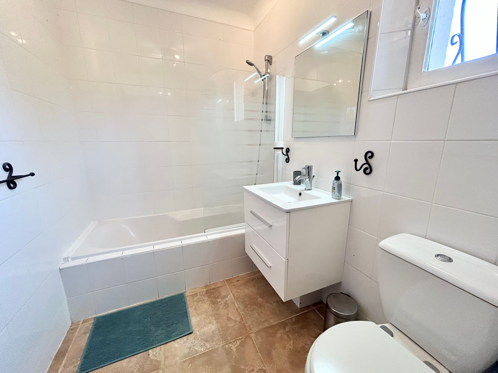 Salle de bain avec murs carrelés blancs, vanité blanche, toilettes et baignoire