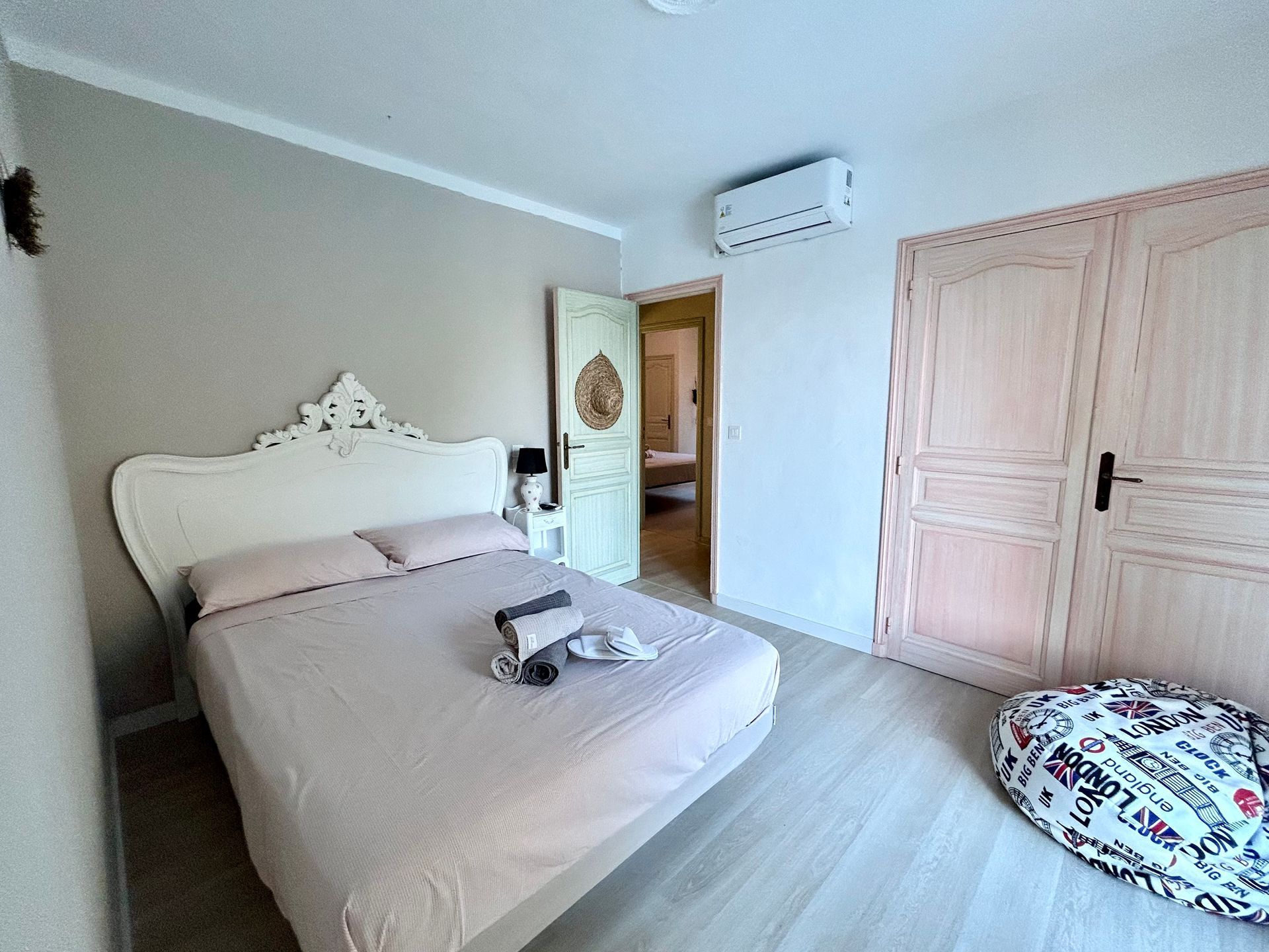 Chambre avec lit, literie rose, tête de lit blanche, parquet en bois clair et porte vert clair.