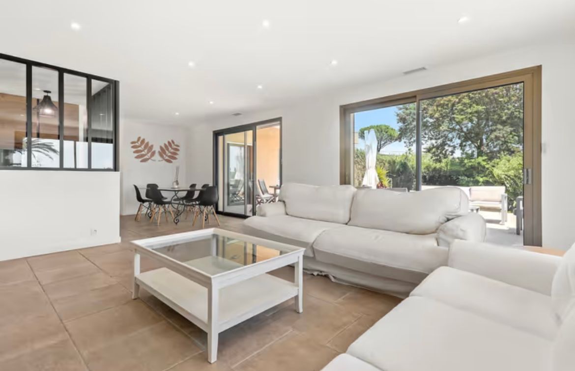 Salon lumineux avec canapé blanc, table basse en verre et portes coulissantes donnant sur l'espace extérieur.