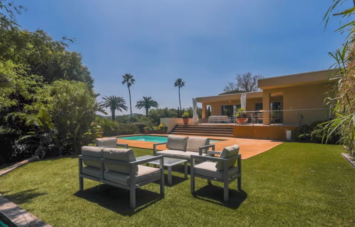 Arrière-cour avec piscine, coin salon et maison moderne sous un ciel bleu.