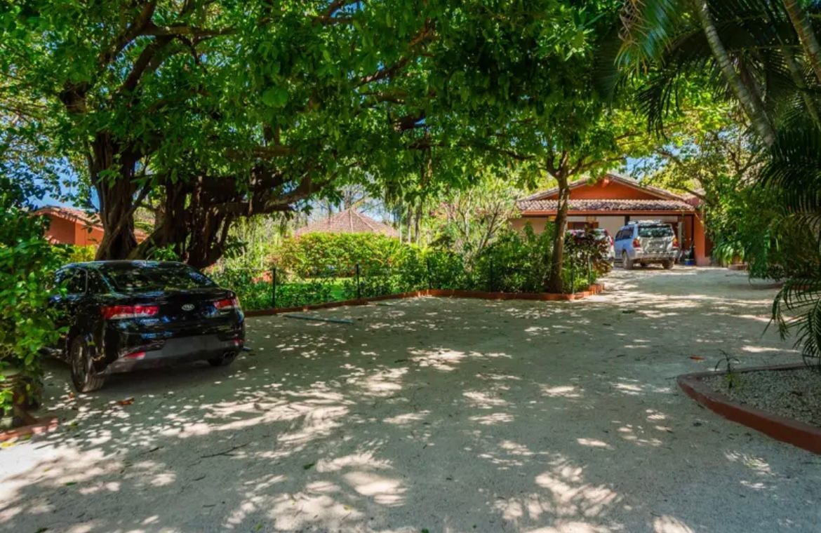 Voiture noire garée dans l'allée d'une maison, ombragée par des arbres.
