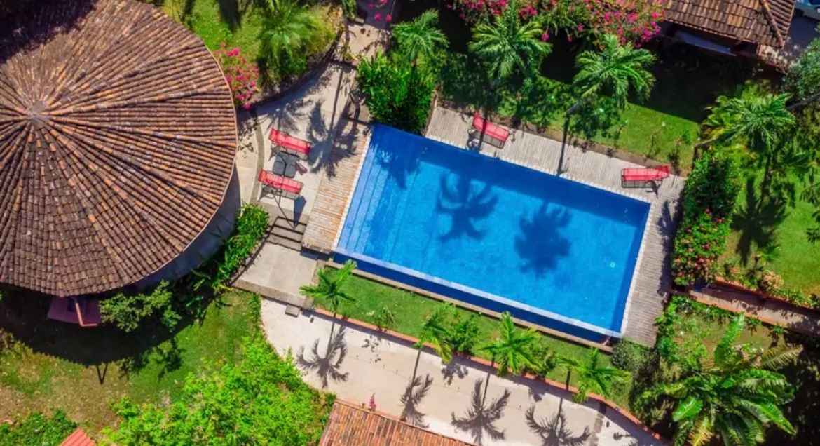 Vue aérienne d'une piscine entourée d'herbe verte, de palmiers et de bâtiments aux toits de tuiles.
