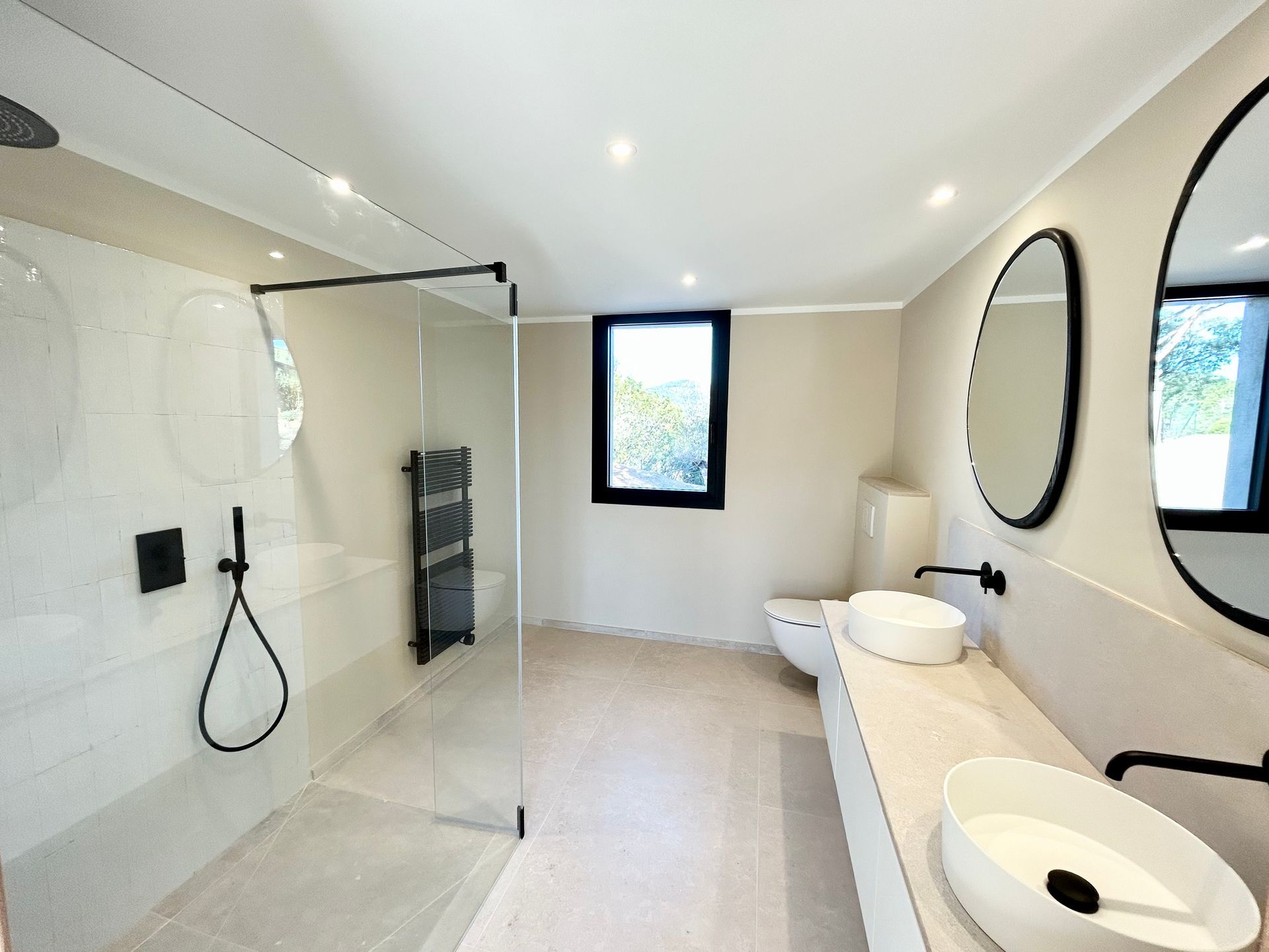 Salle de bain moderne avec douche à l'italienne, double vasque et fenêtre. Robinetterie noire et tons neutres.