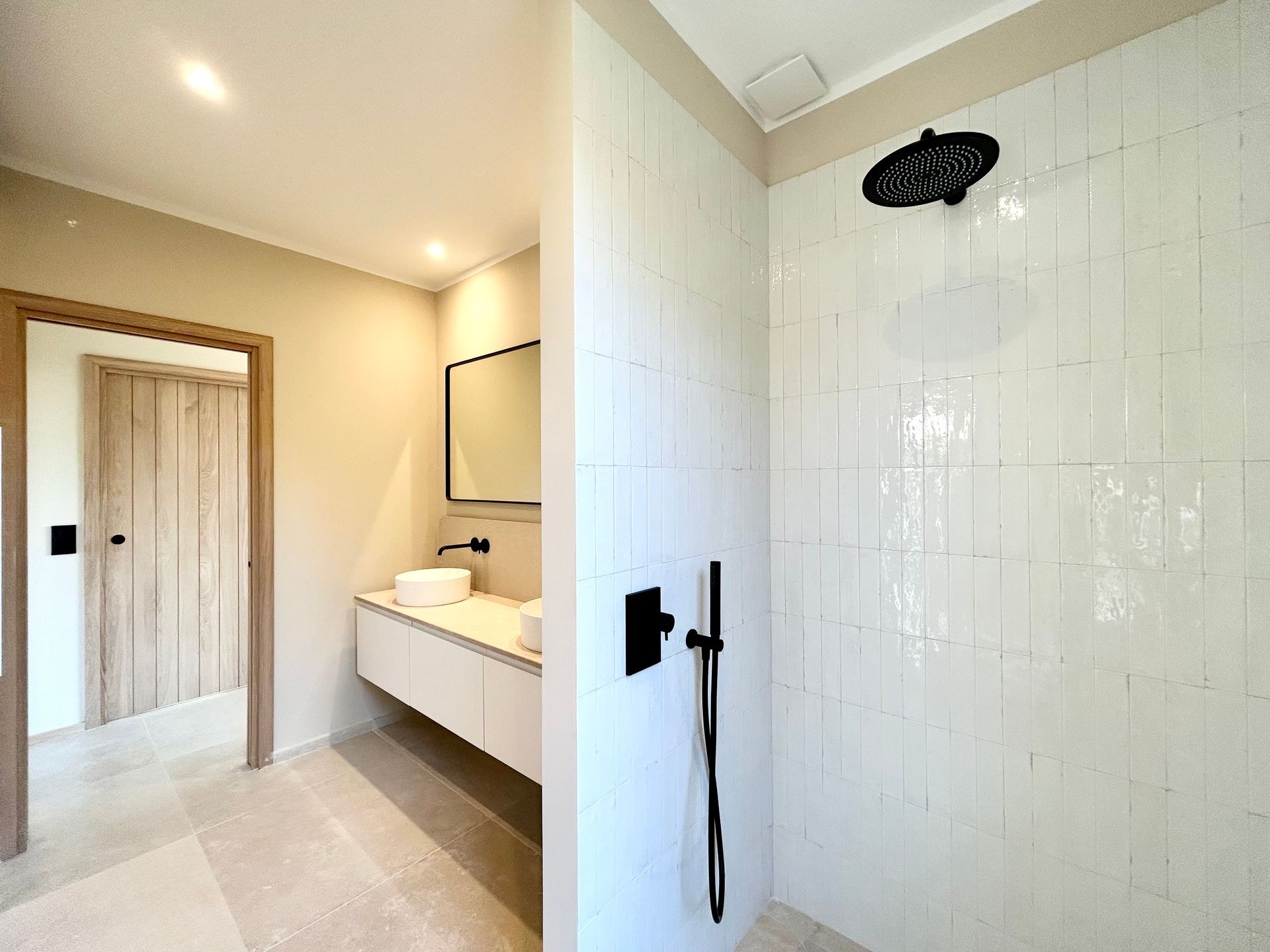 Salle de bain moderne avec douche en carrelage blanc, luminaires noirs et vanité.