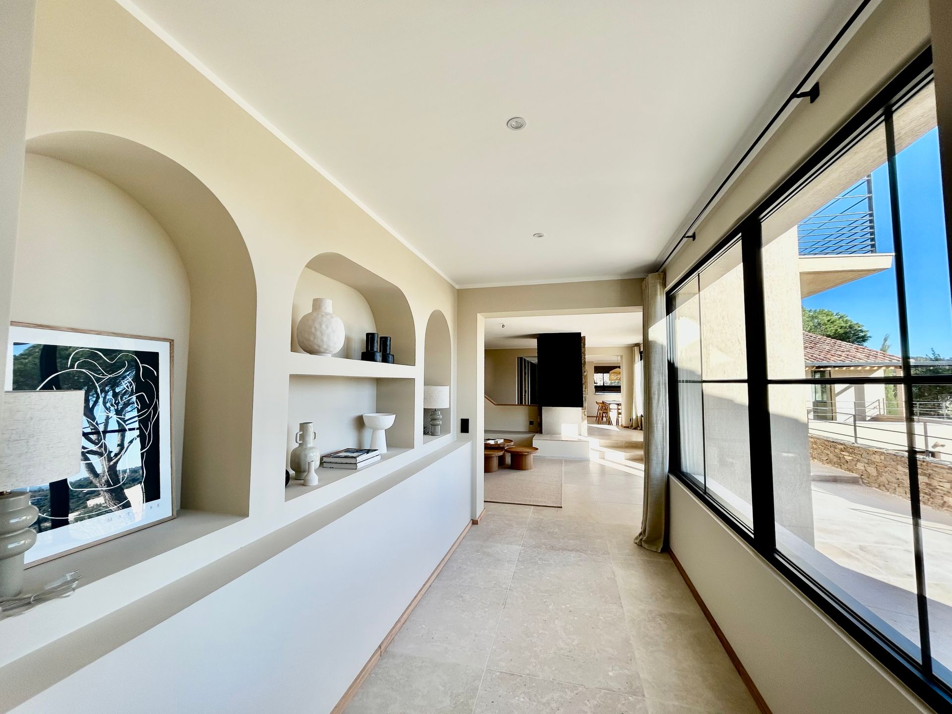 Couloir avec niches cintrées et grandes fenêtres, tons beige et blanc.