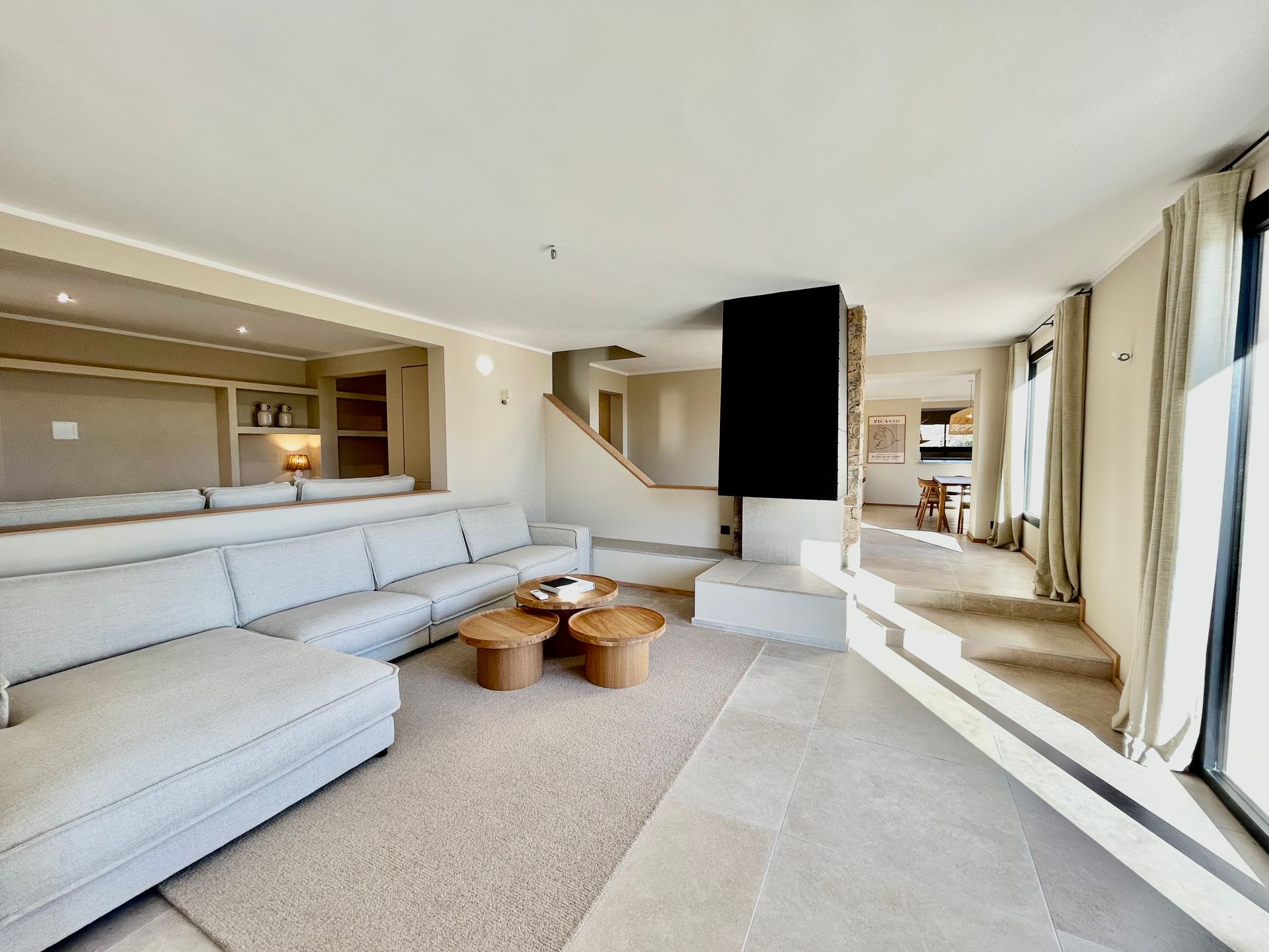 Salon moderne avec canapé sectionnel beige, tables basses et cheminée ; des marches mènent à la salle à manger.