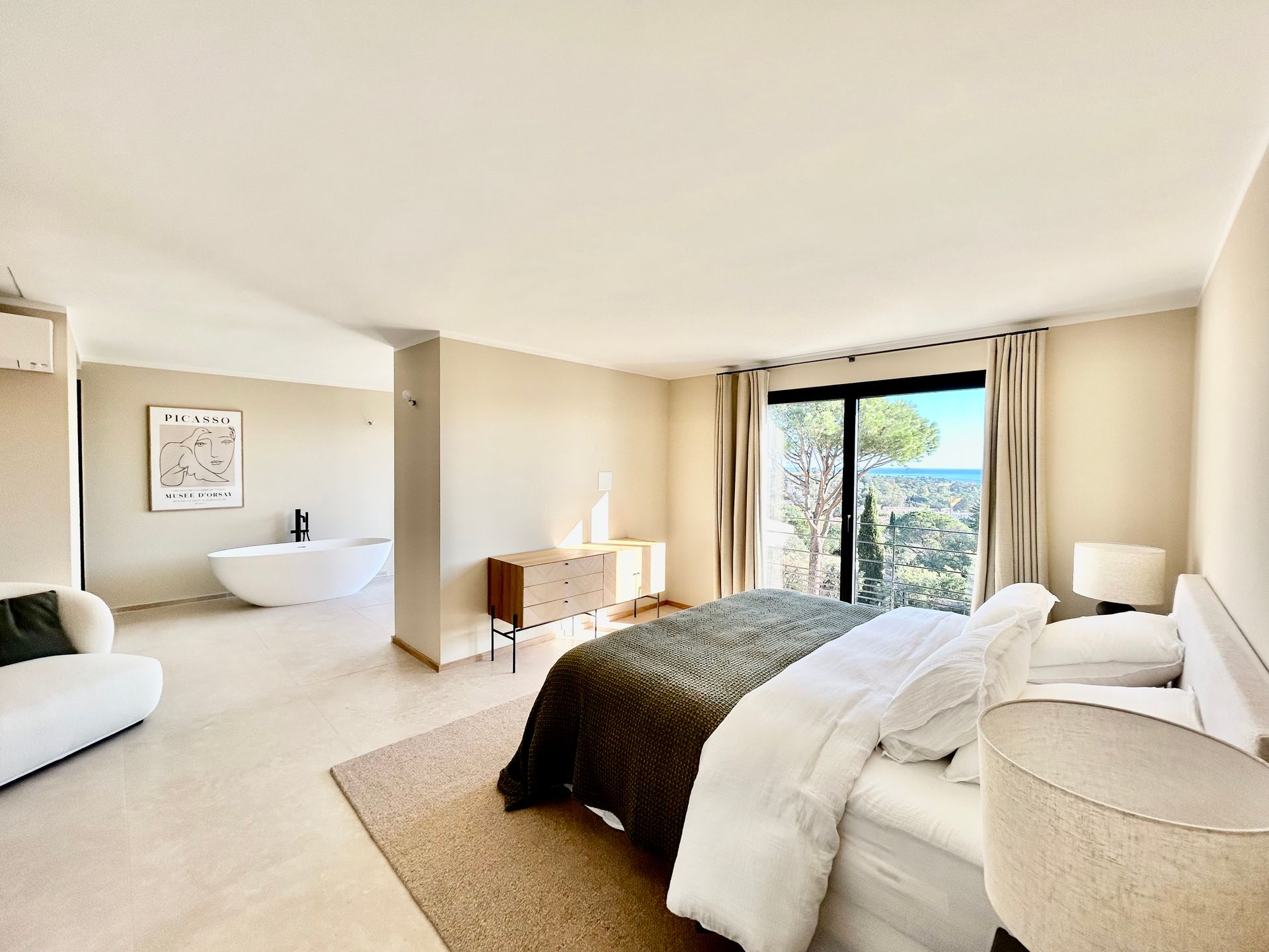 Chambre spacieuse avec un lit, une salle de bain ouverte et une vue panoramique à travers des portes vitrées.