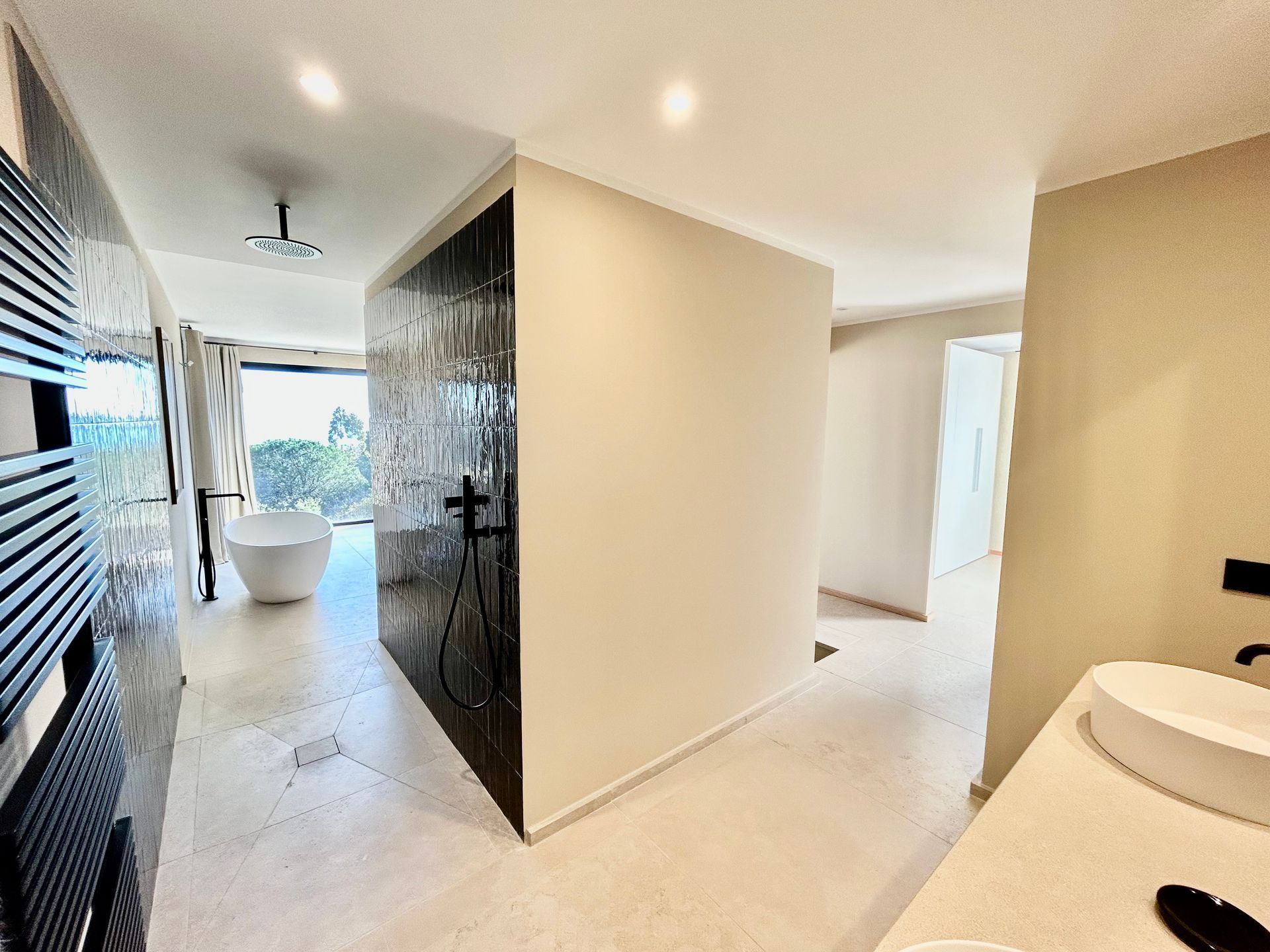 Salle de bain moderne avec baignoire, douche et lavabo. Murs et sol blancs, avec des touches de motifs sombres.