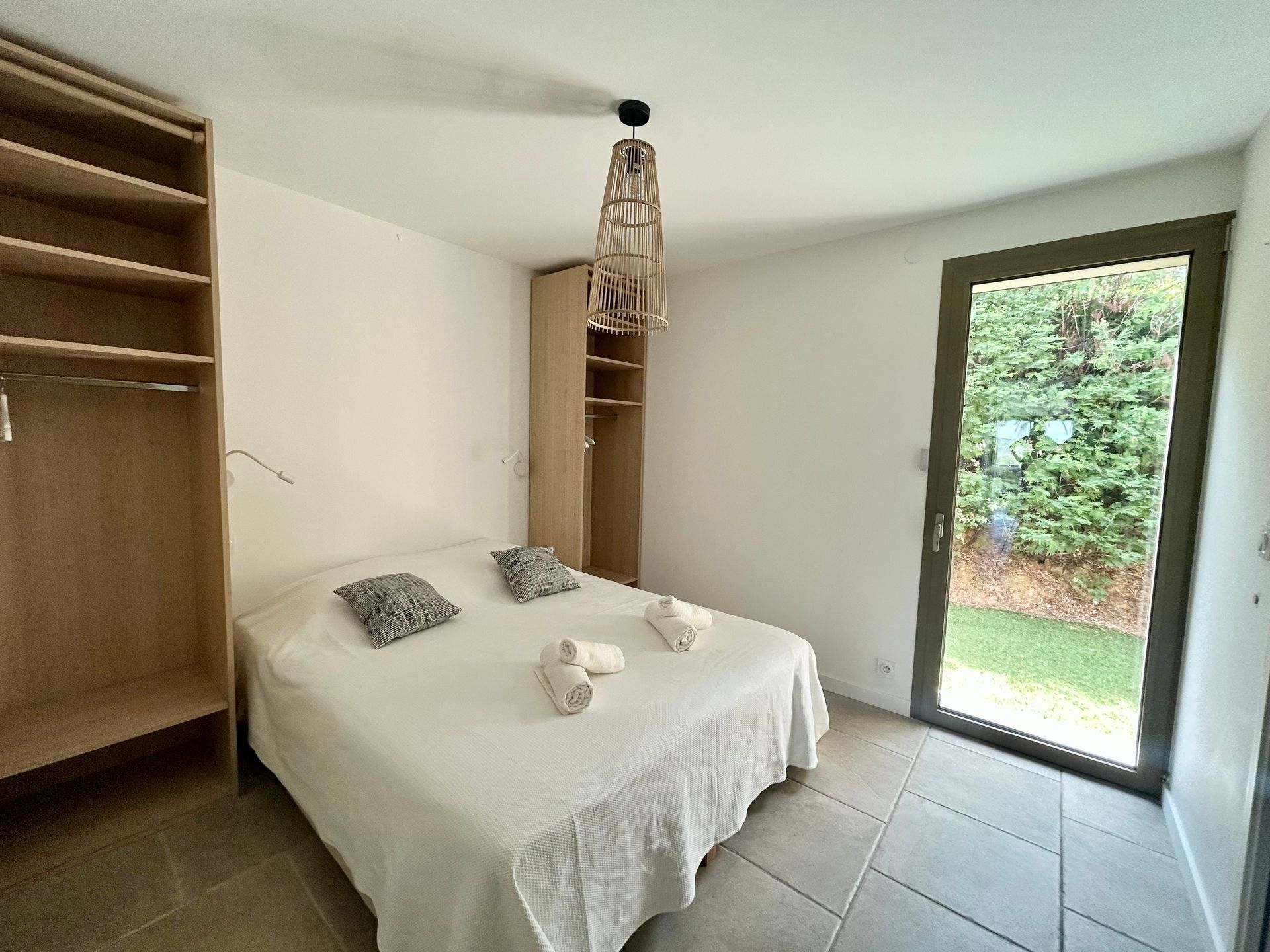 Chambre avec lit, placard et porte donnant sur un jardin.