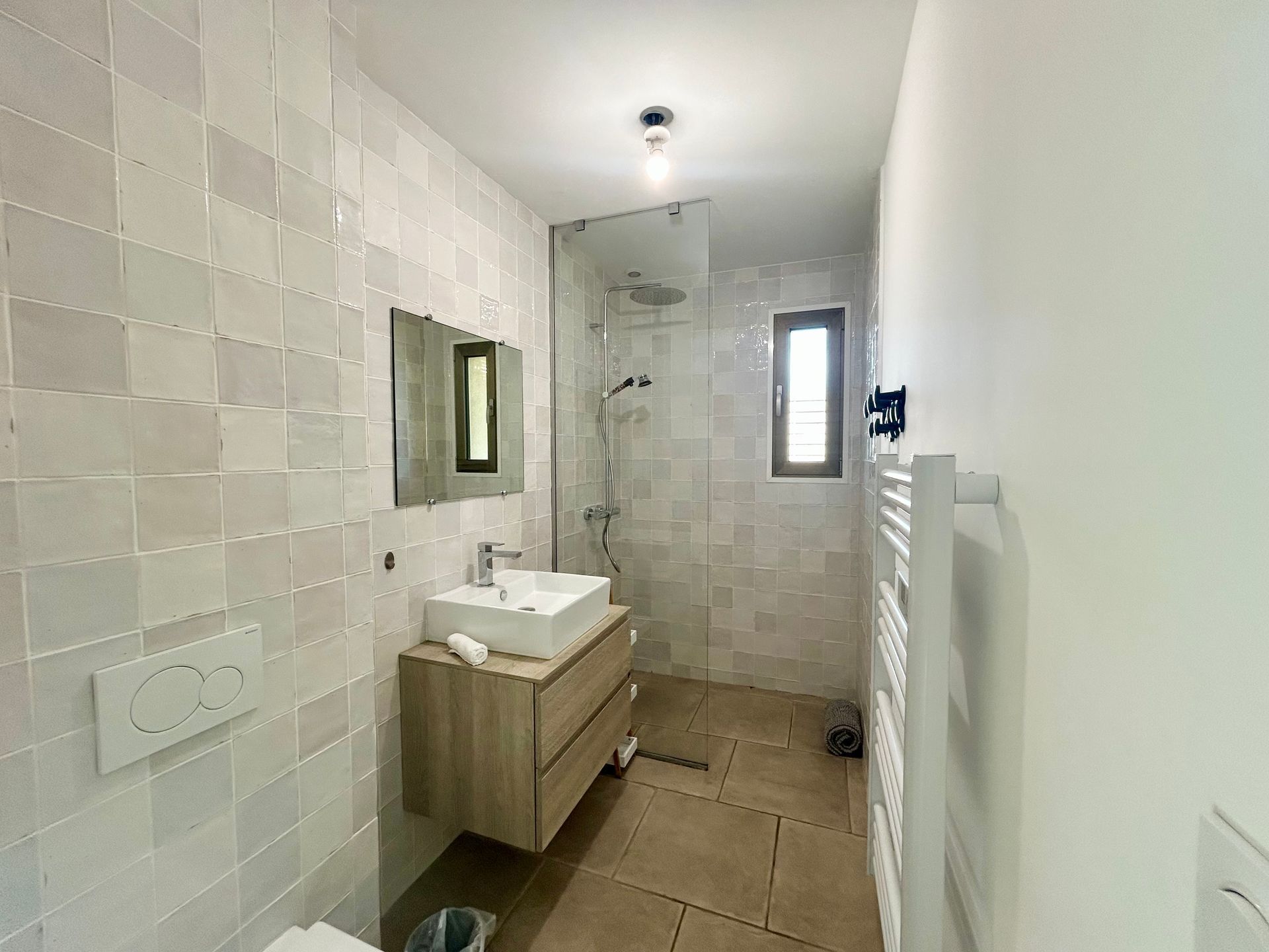 Salle de bain moderne avec murs en carrelage carré, vanité en bois et douche en verre.