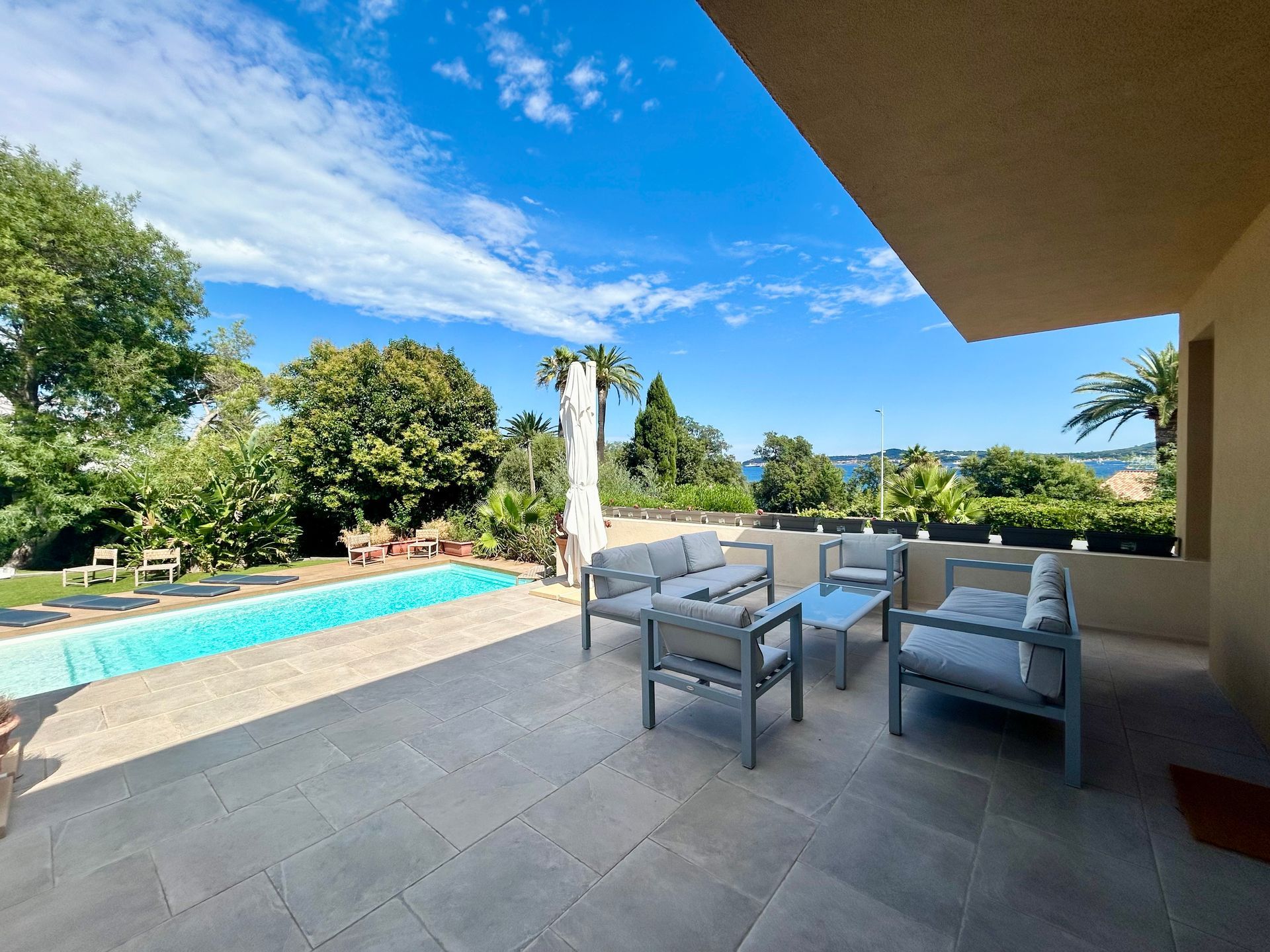 Patio avec sièges, piscine, aménagement paysager luxuriant et ciel bleu surplombant la mer.