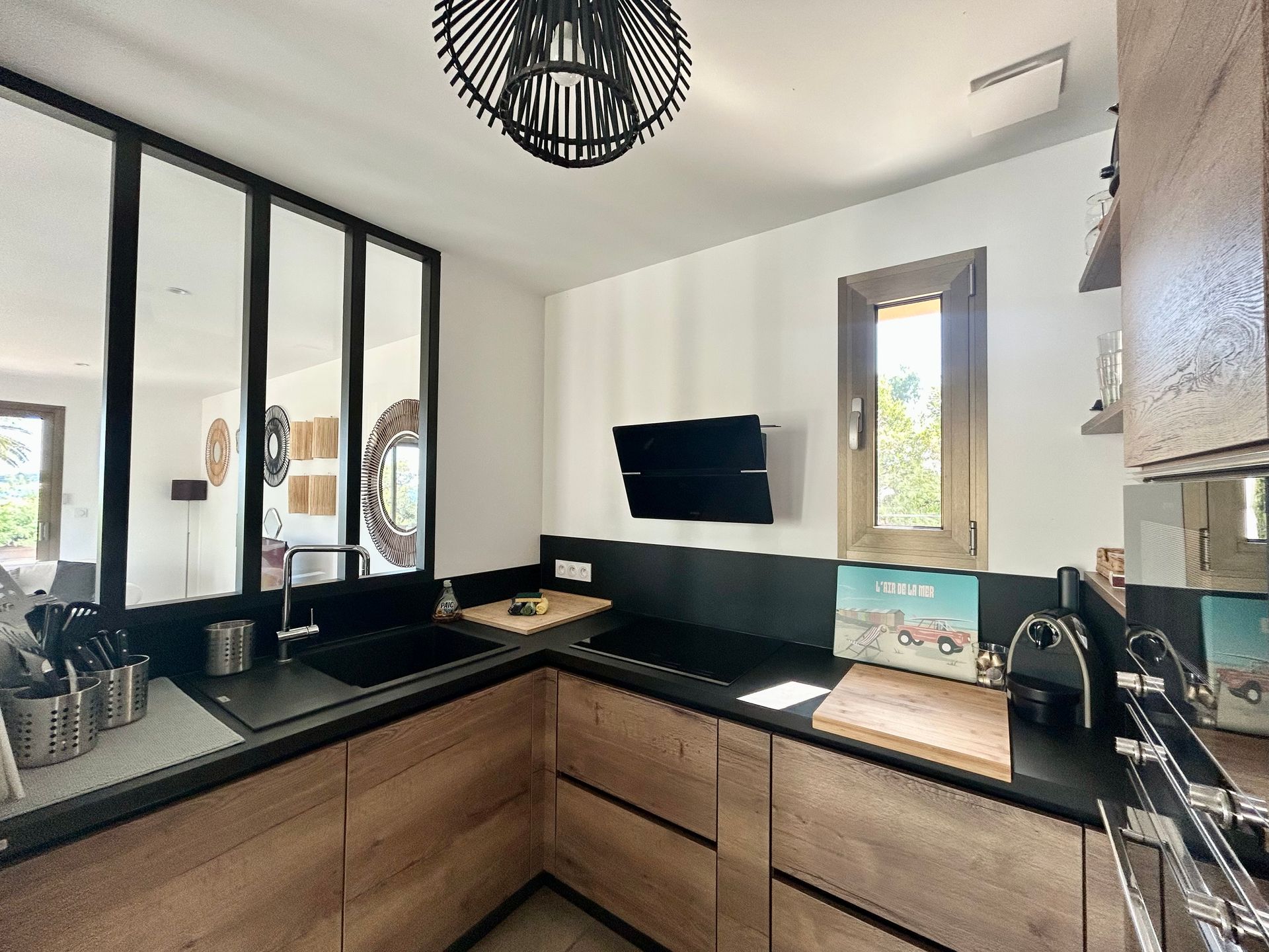 Cuisine moderne avec armoires en bois, comptoirs noirs et fenêtre.