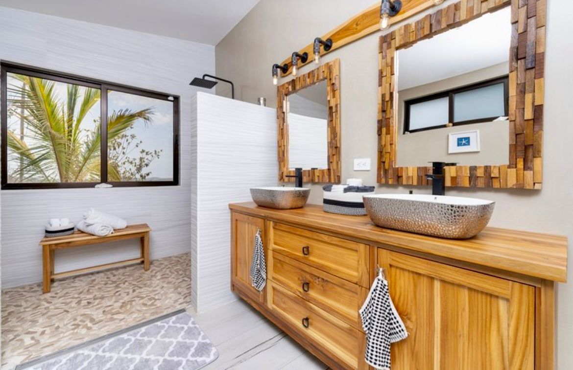 Salle de bain avec meuble-lavabo en bois, vasques argentées et sol en mosaïque.