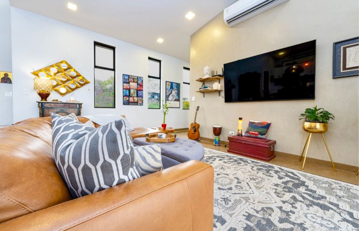 Salon avec canapé en cuir, télévision, art, guitare et tapis à motifs.