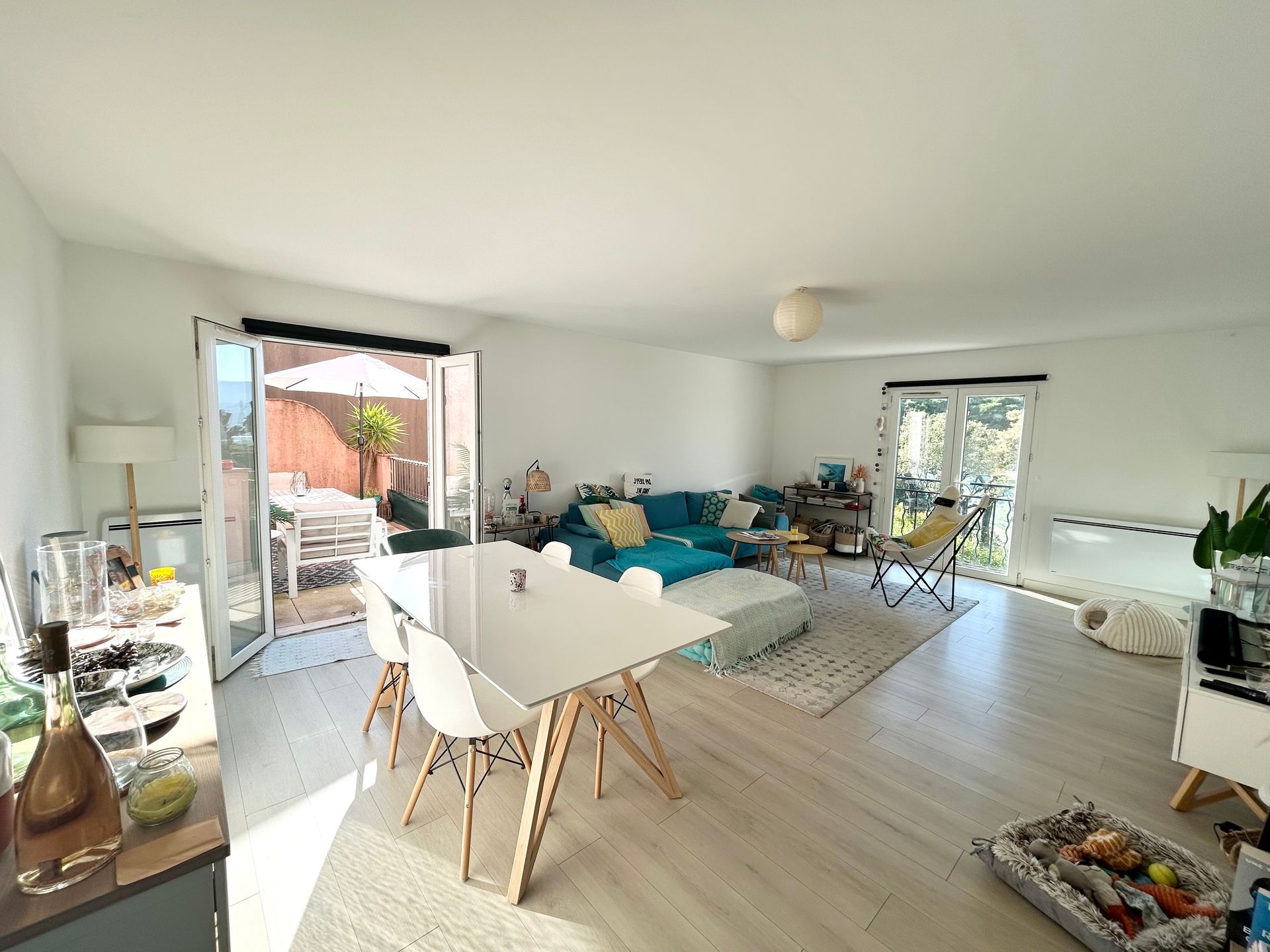 Salon lumineux avec table à manger, canapé bleu sarcelle et portes donnant sur le patio.