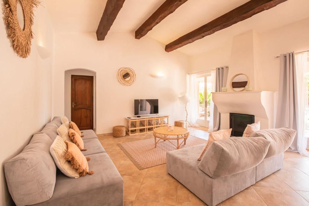 Salon avec canapés gris, poutres en bois et cheminée.