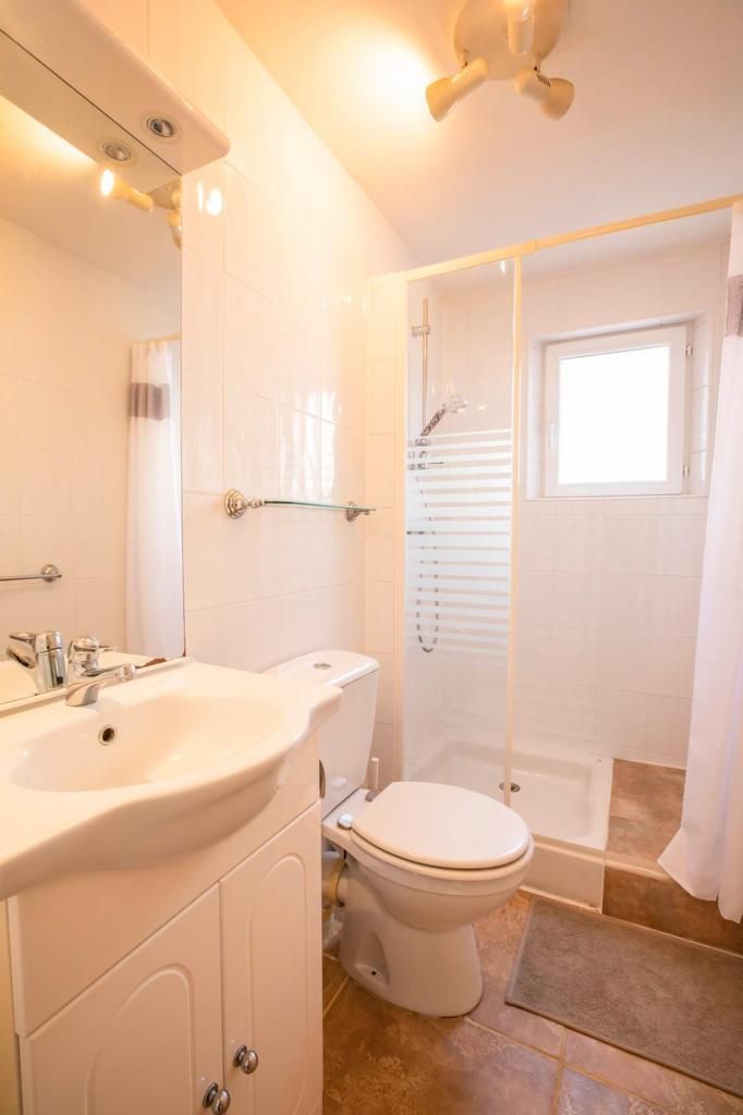 Salle de bain blanche avec toilettes, lavabo et douche.