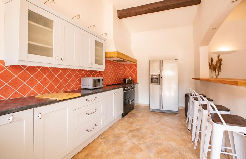 Cuisine avec armoires blanches, dosseret en carrelage orange et bar à déjeuner avec tabourets.