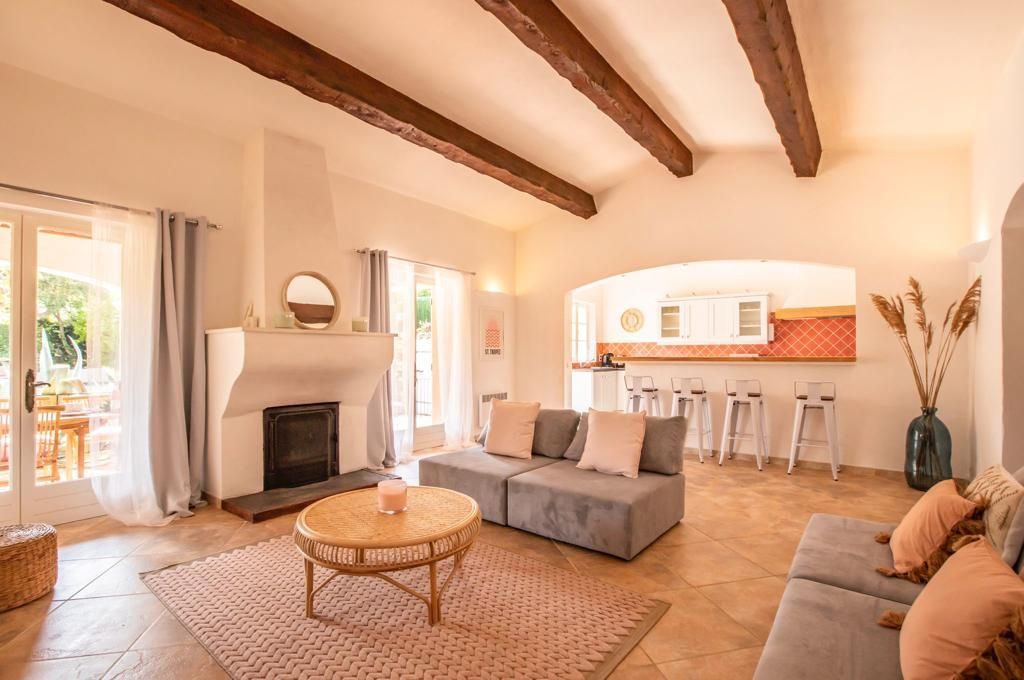 Séjour avec cheminée, canapés et cuisine ouverte avec tabourets de bar, tons beige et marron.