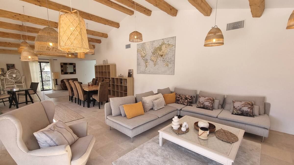 Un salon spacieux avec un canapé sectionnel gris, un coin repas et un plafond avec poutres en bois.