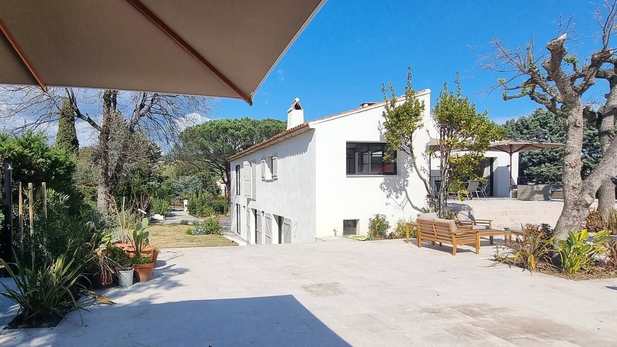 Maison blanche avec patio et arbres, par une journée ensoleillée.