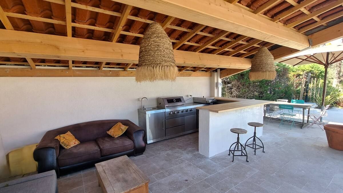 Cuisine extérieure avec canapé marron, bar, grill sous un patio couvert.