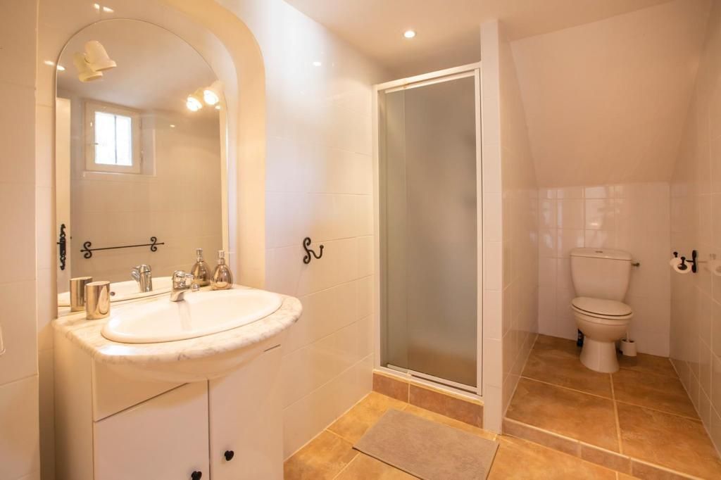 Salle de bains avec lavabo, douche et toilettes, le tout blanc, avec un sol carrelé beige.