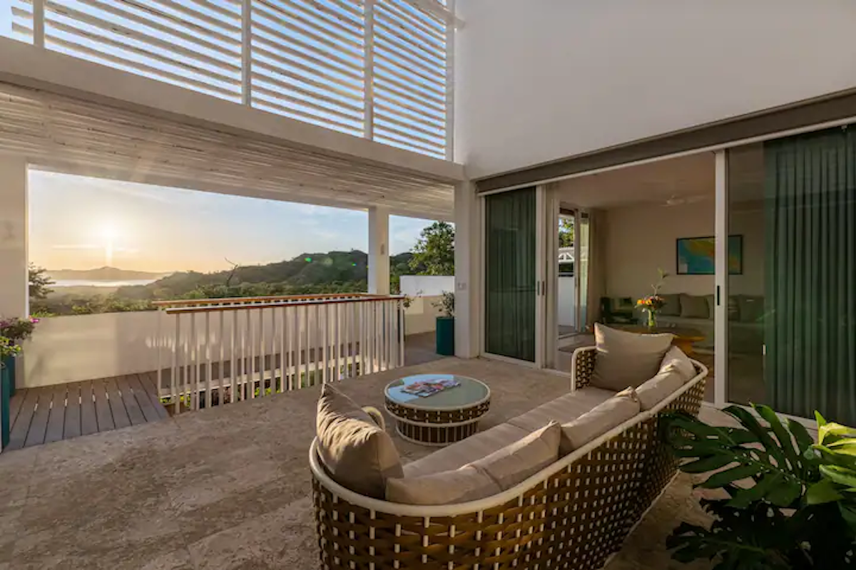 Terrasse extérieure avec vue panoramique, canapé tissé beige et portes coulissantes en verre.