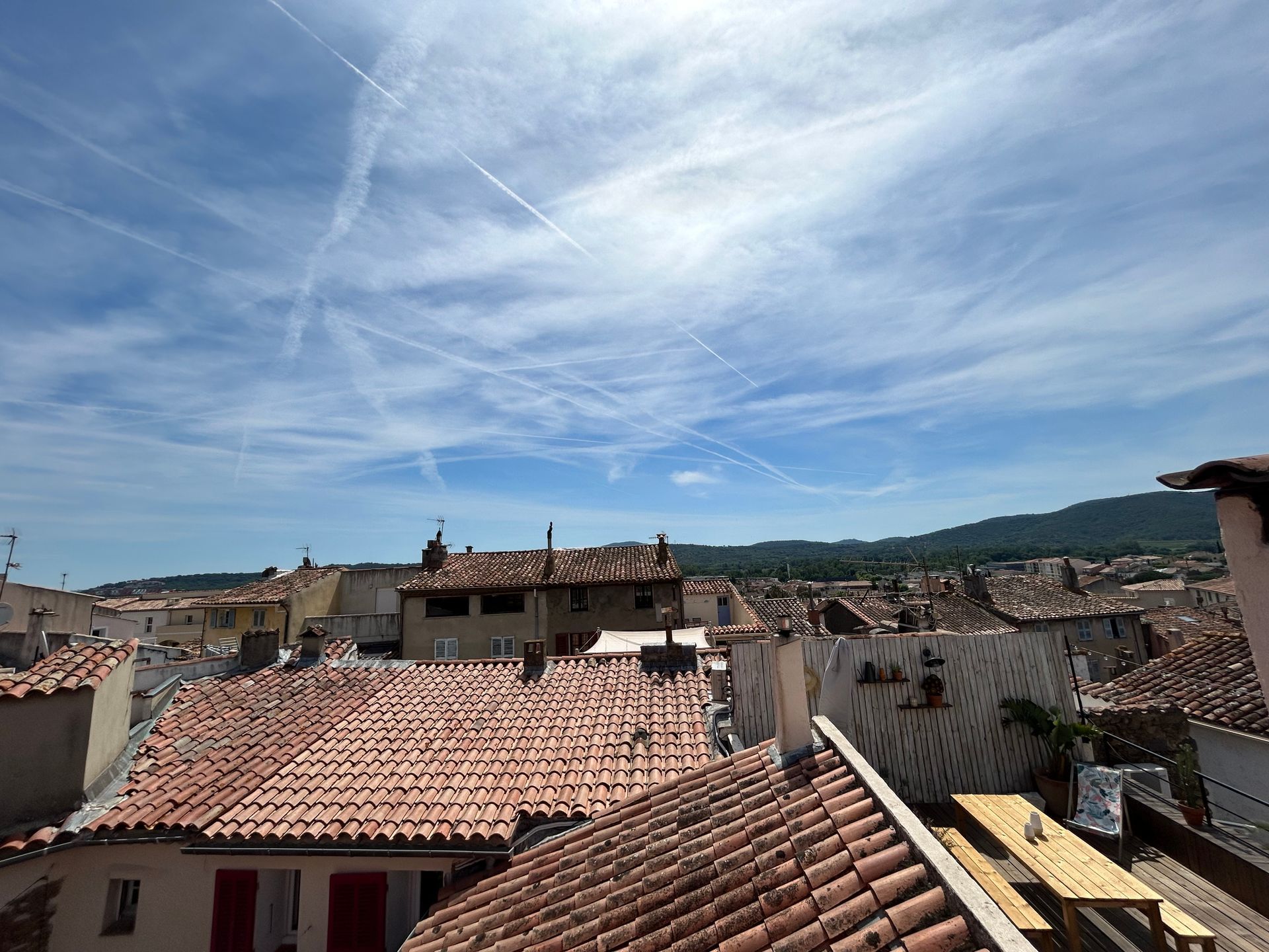Vue du toit d'une ville aux toits de tuiles rouges, sous un ciel bleu vif avec des traînées de condensation.