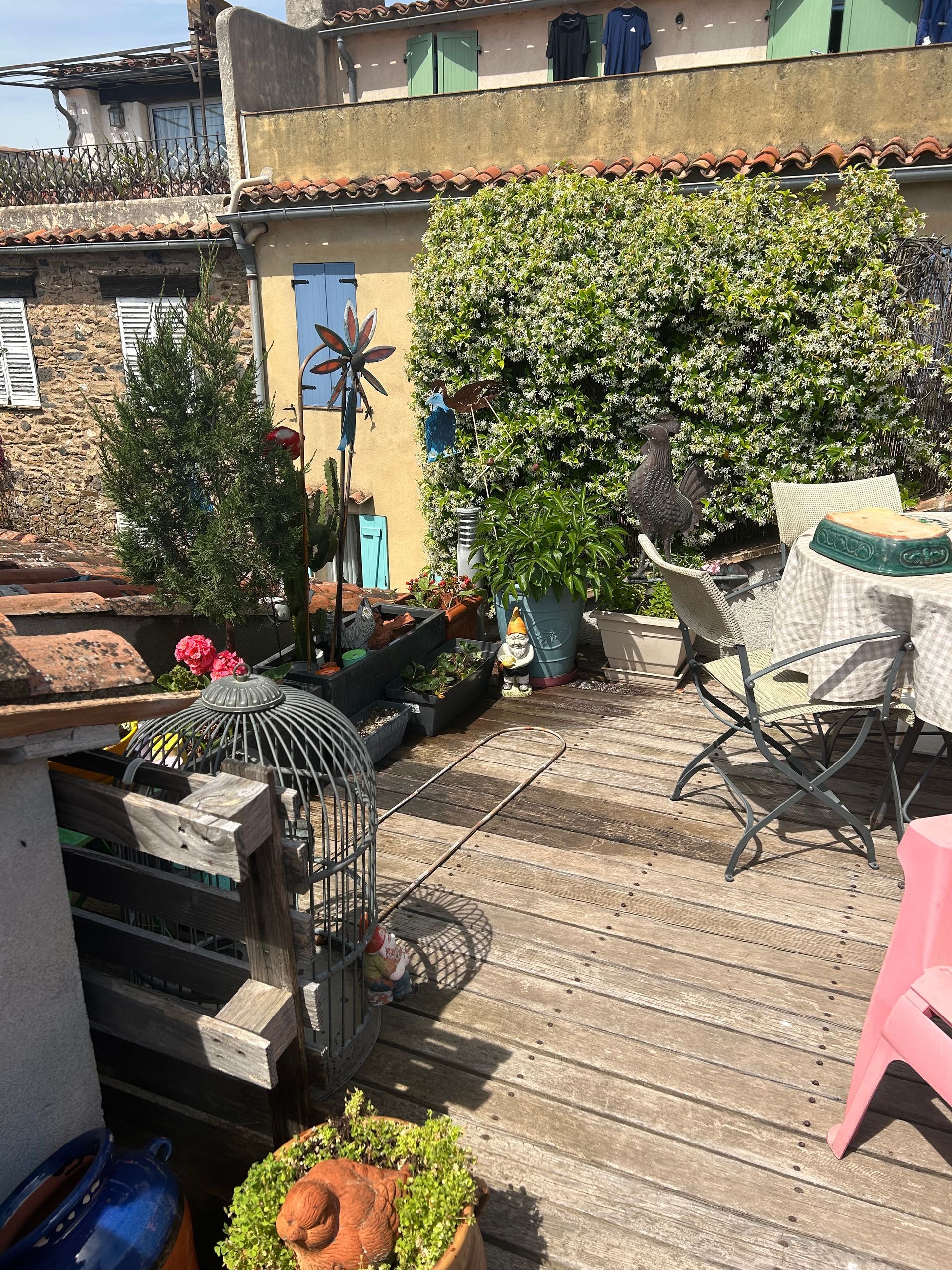 Terrasse sur le toit avec plantes, meubles et bâtiment en arrière-plan sous un ciel ensoleillé.