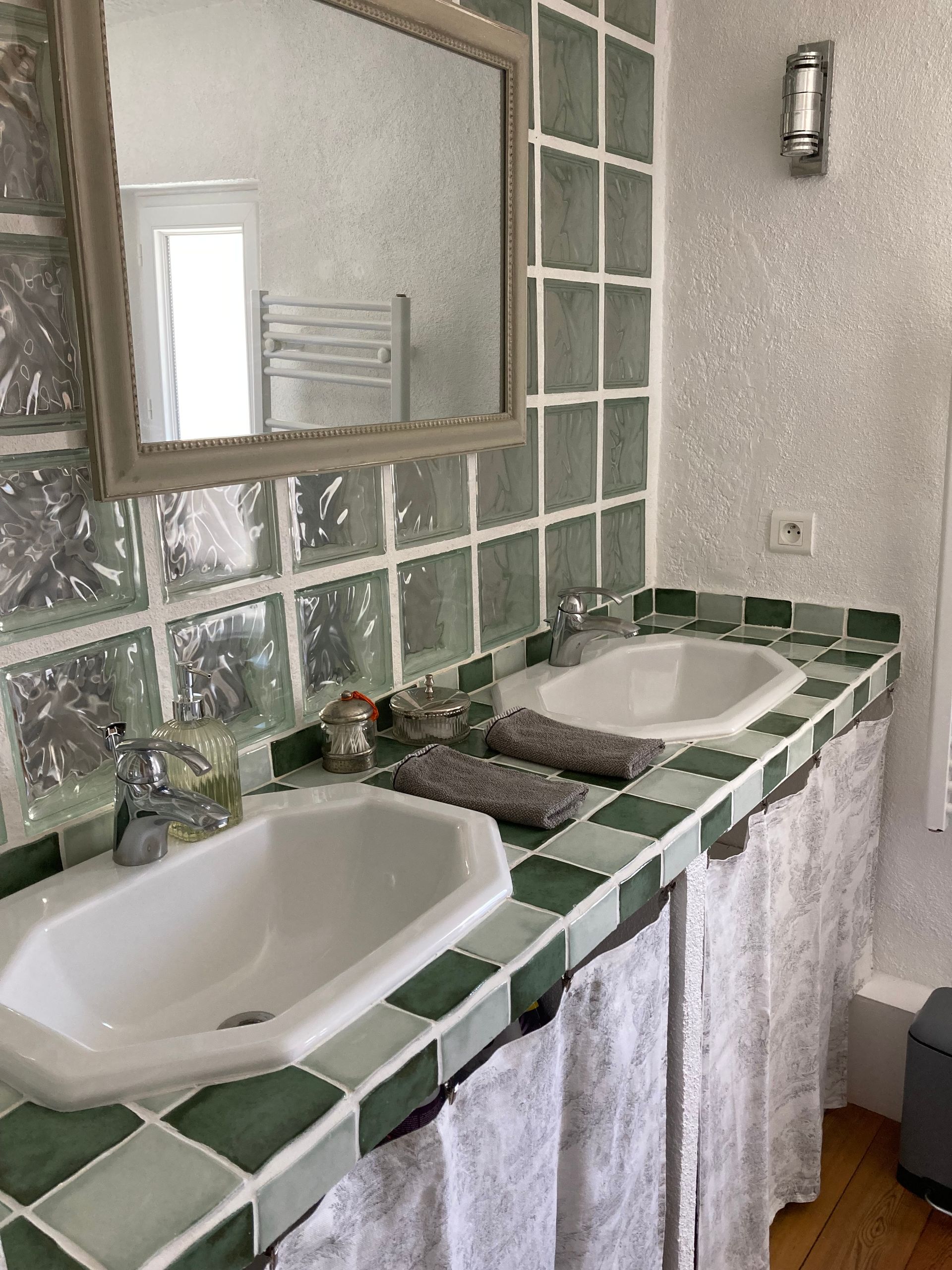 Salle de bain avec deux lavabos, un grand miroir et des surfaces carrelées vertes et blanches.