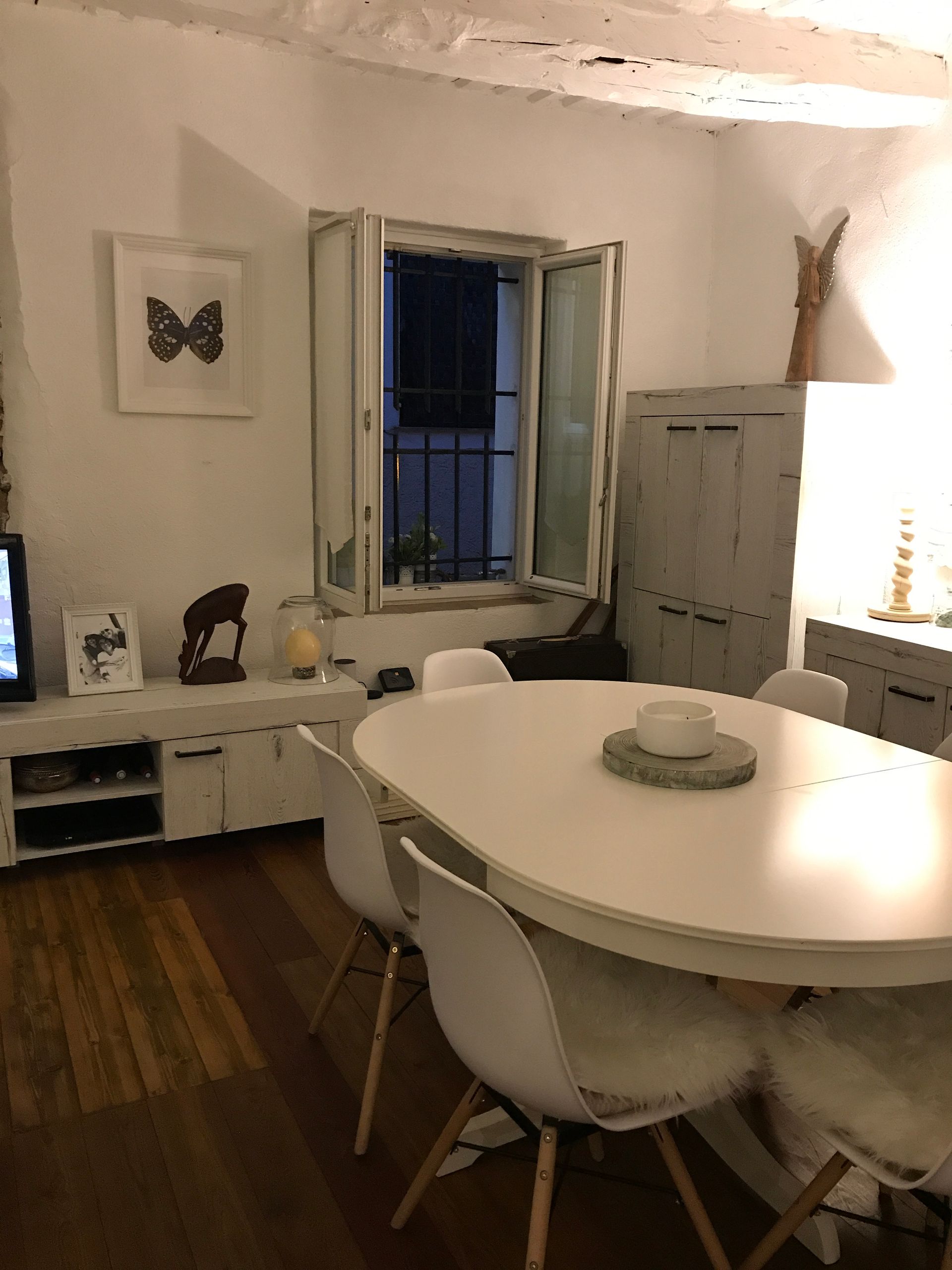 Salle à manger avec table ovale blanche, chaises modernes, fenêtre et art mural.
