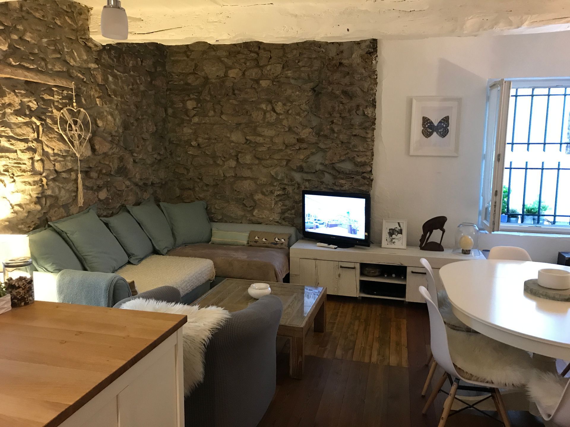 Salon avec mur en pierre, canapé sectionnel, télévision et table à manger près d'une fenêtre.