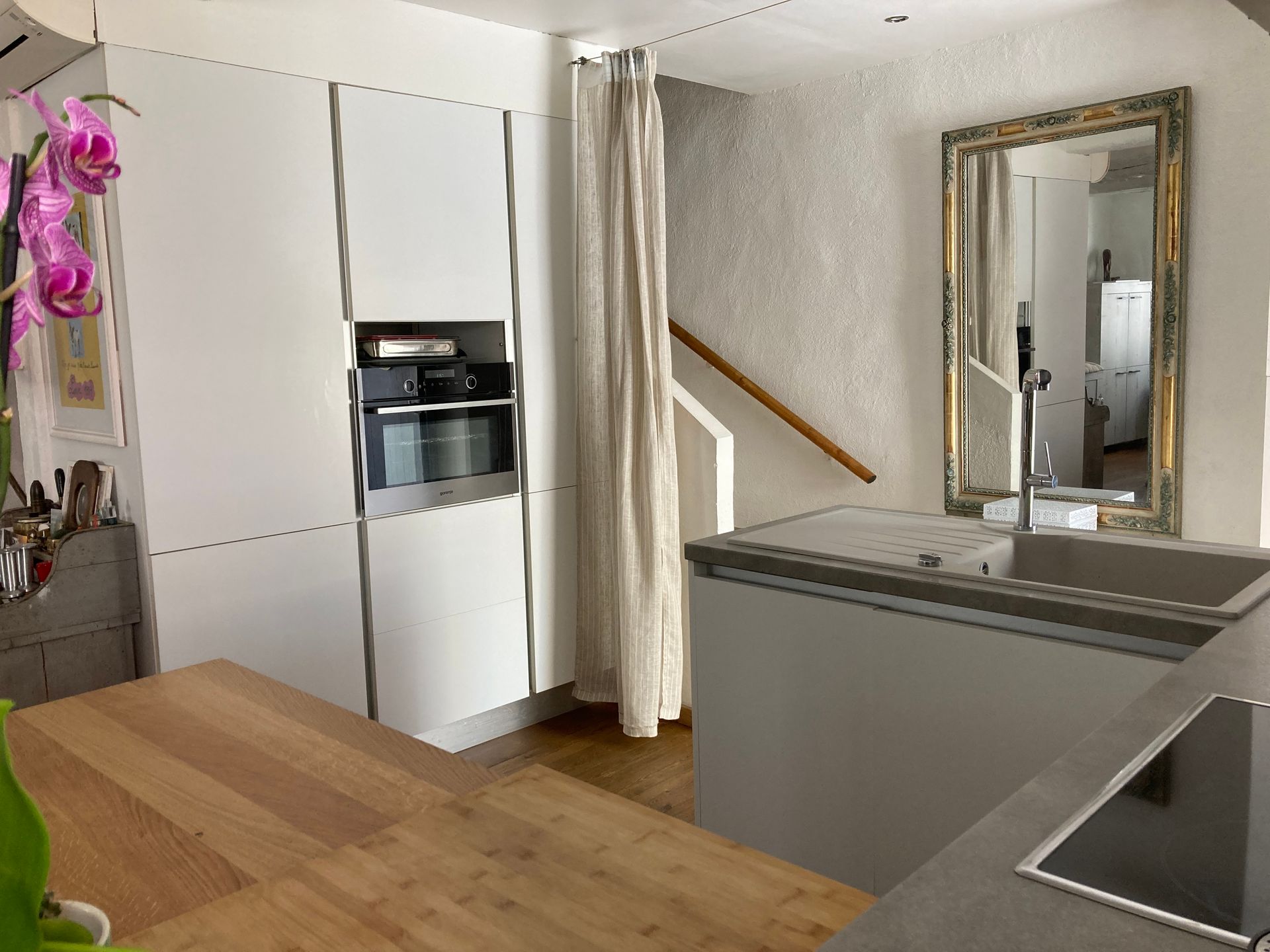 Cuisine moderne avec armoires blanches, une table en bois et un grand miroir.