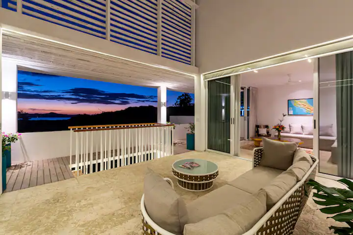 Balcon avec canapé beige incurvé, donnant sur une vue au crépuscule.